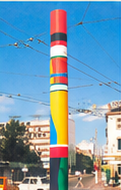 Haute colonne polychrome dressée sur une place, sous des fils de tramway